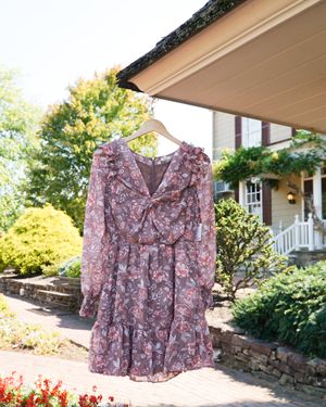 Floral print maxi dress with long sleeves and ruffled details hanging outside a stone building.
