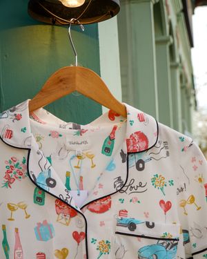 Fun printed pajama top with champagne bottles, cars, and hearts hanging on a wooden hanger.