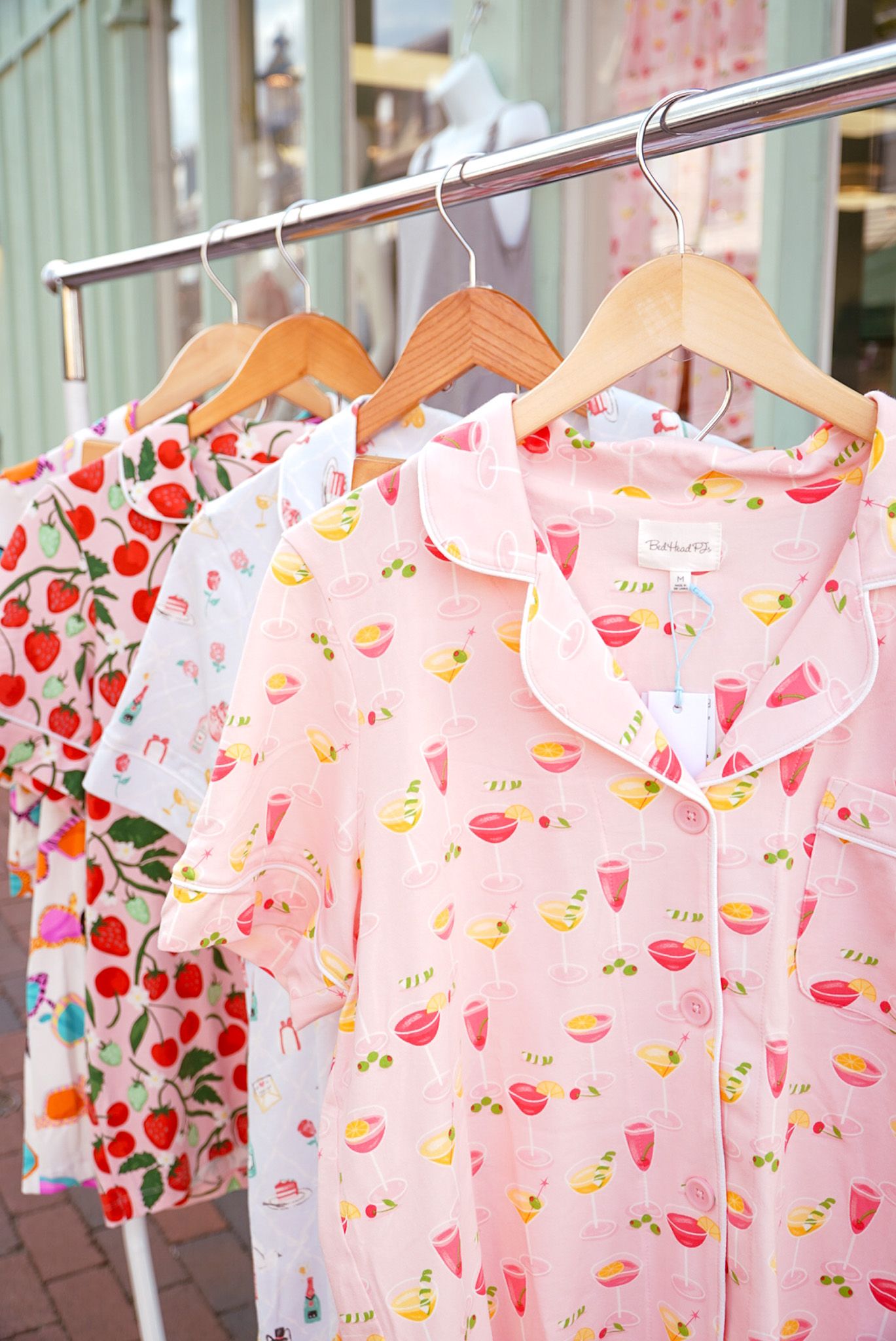Colorful summer dresses with fruit prints hanging on wooden hangers in a boutique display.