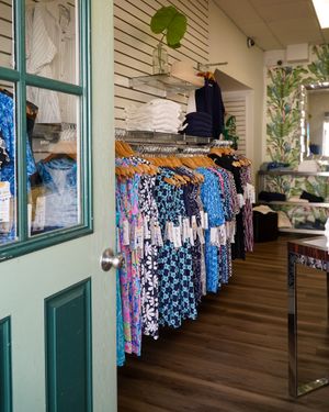 Colorful dresses and clothing displayed on racks at a boutique store with green trim windows.