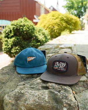 Two baseball caps, one blue and one gray, sitting on a rock outdoors.
