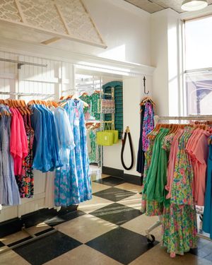 Colorful summer dresses and clothing arranged on racks in a boutique with black and white tiled floors.