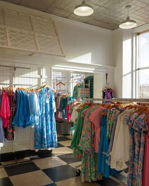 Bright floral and patterned dresses displayed in a retail store with checkered floor and natural lighting.
