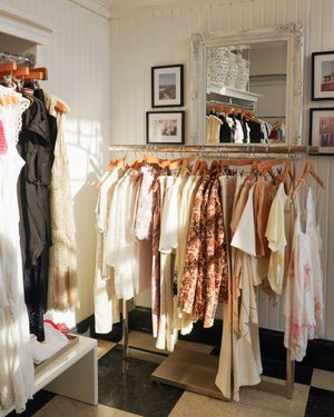Elegant white and floral dresses displayed on wooden hangers in a boutique with mirrored walls.