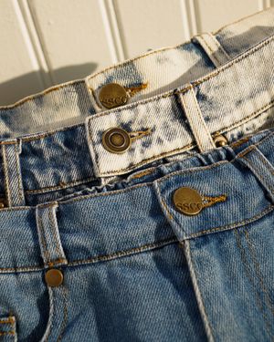 Close-up detail of denim waistband with metal buttons and rivets.