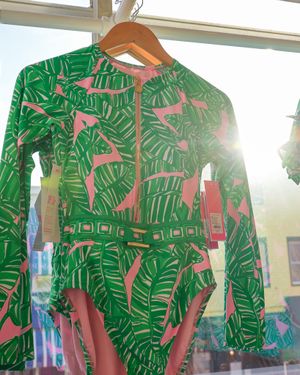 Green and pink tropical print dress hanging in sunlit store window.