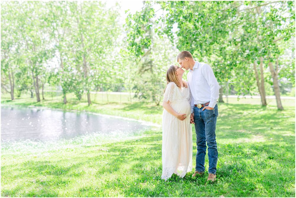 Tender moment between couple during spring maternity photoshoot in park setting by water.