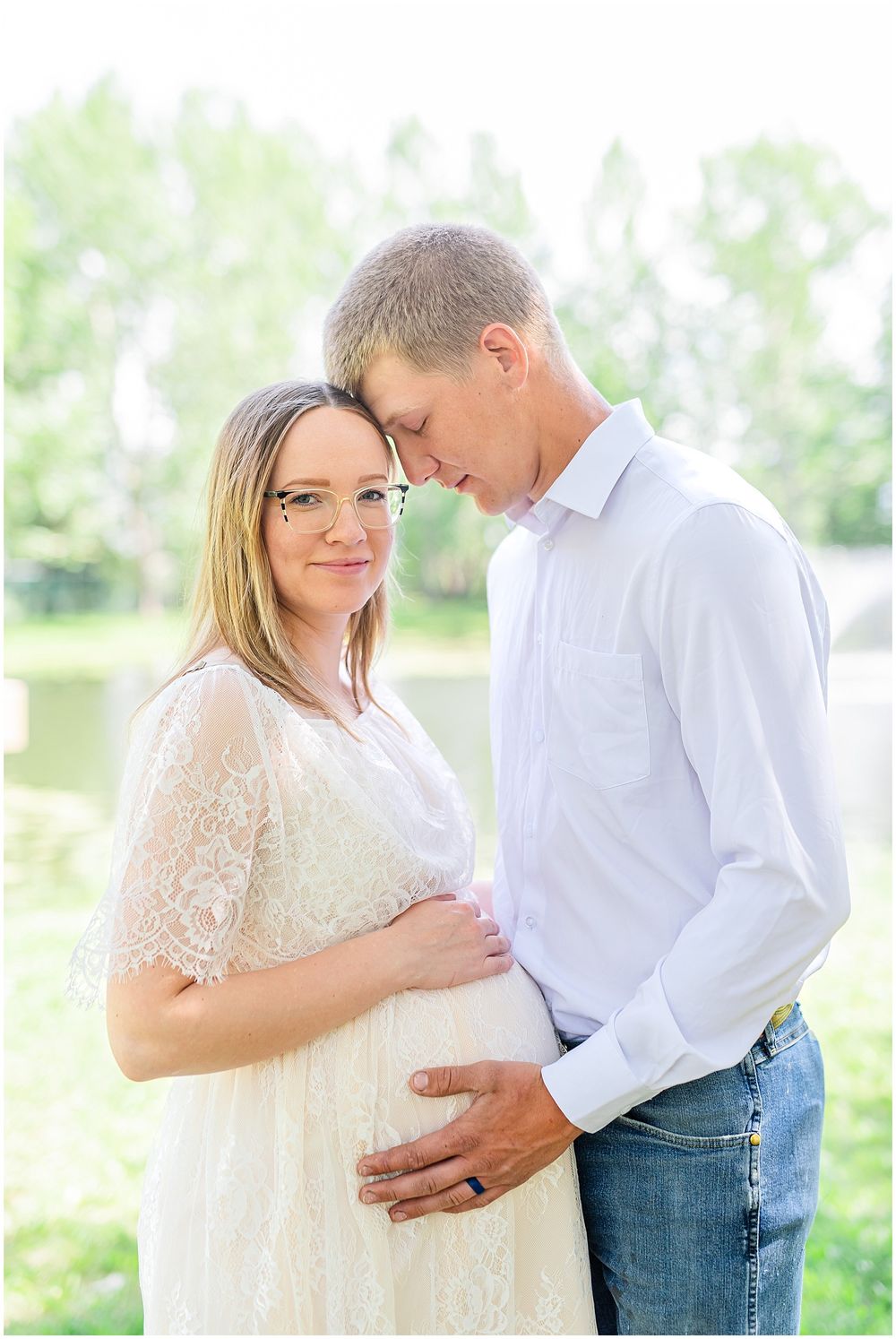 Intimate maternity portrait with couple in white and casual attire against spring foliage.