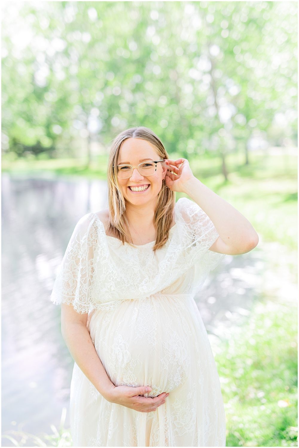 Joyful maternity portrait in a white lace dress against spring foliage.