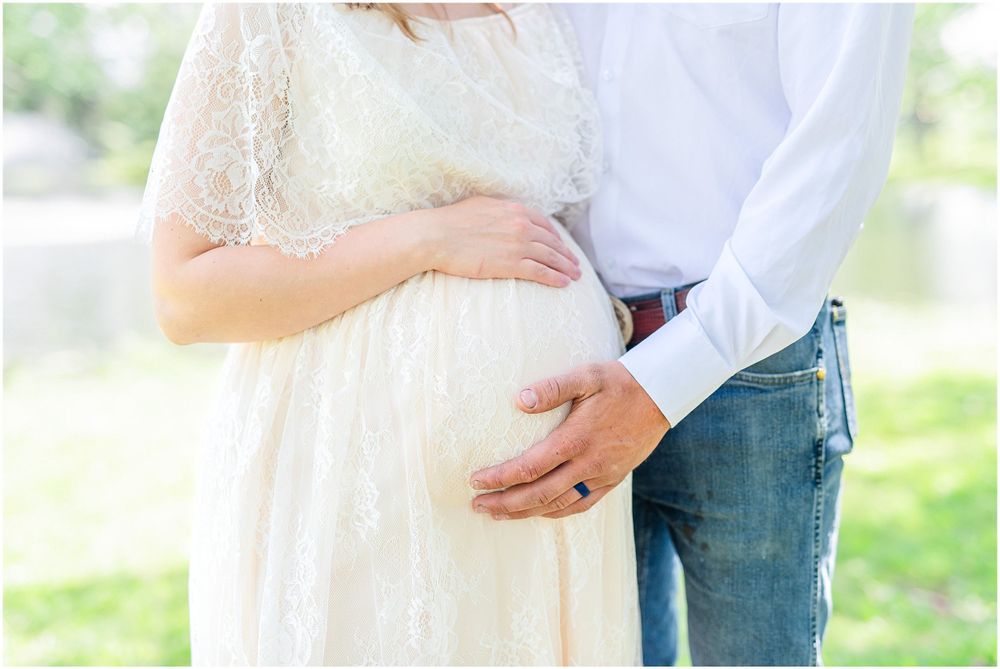 A tender moment captured as hands rest on a baby bump in a sunlit garden setting. Light & airy photography style.