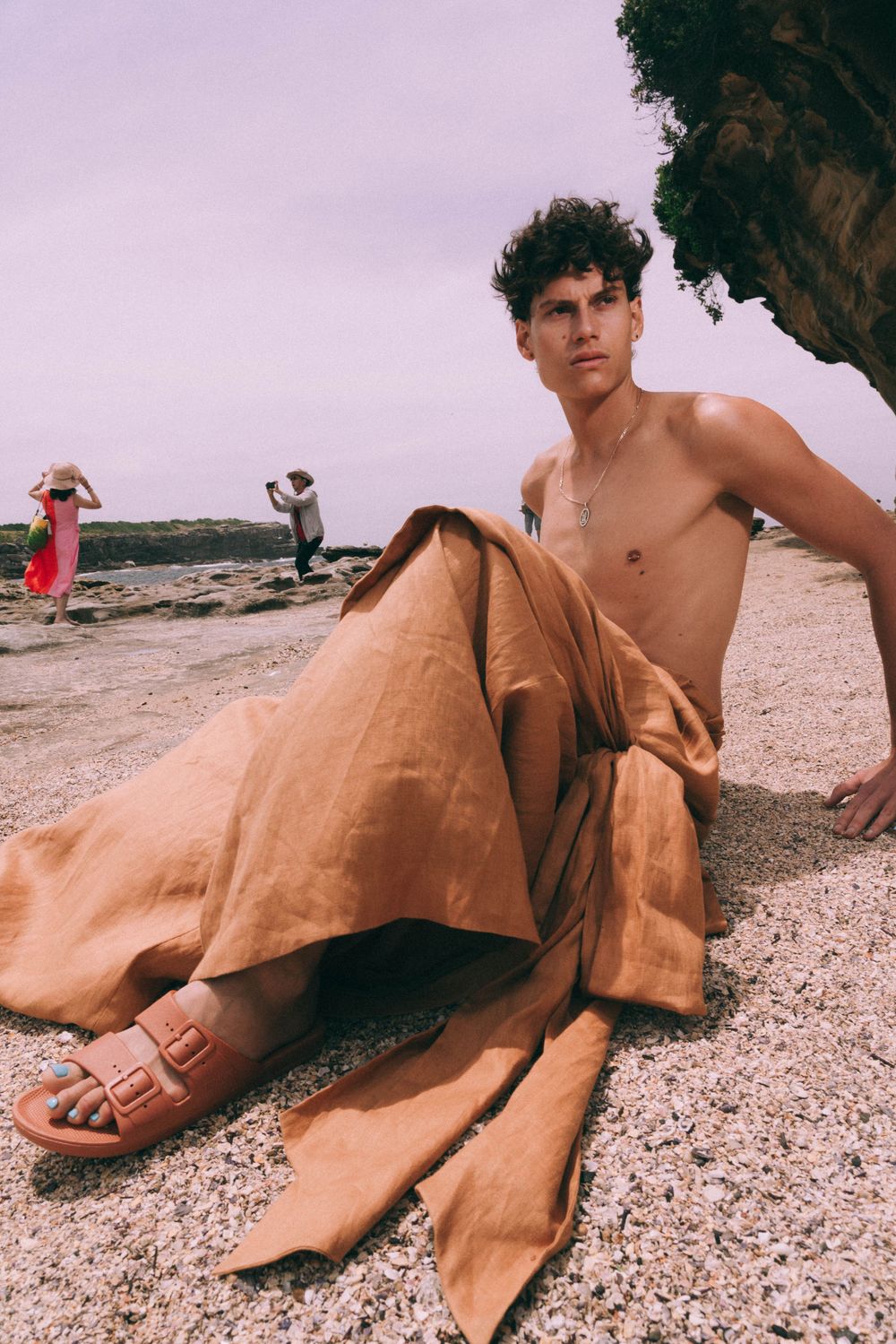 Person in tan pants relaxing on rocky beach with casual summer attire.