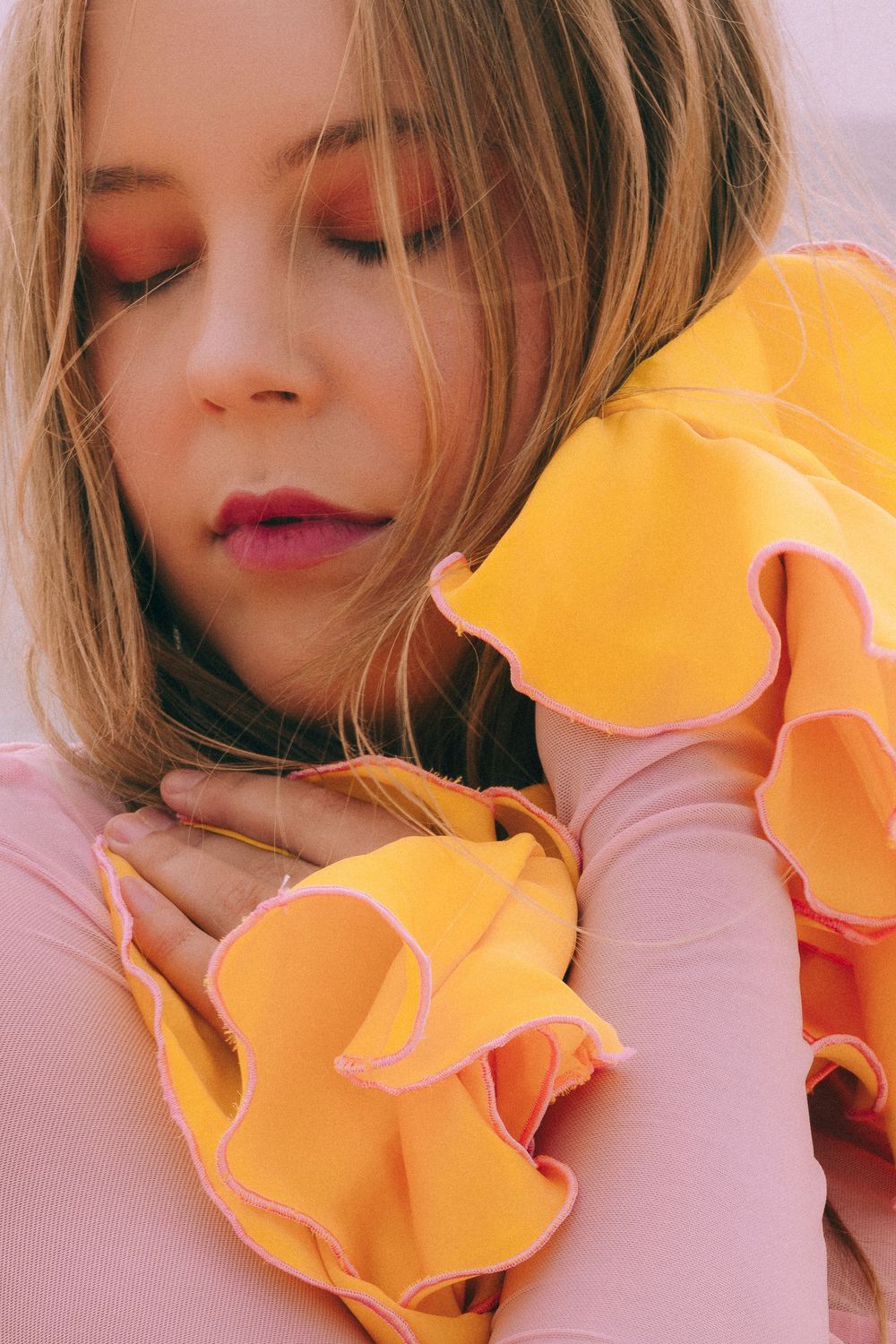 Close up portrait with orange ruffled fabric details against pink background.