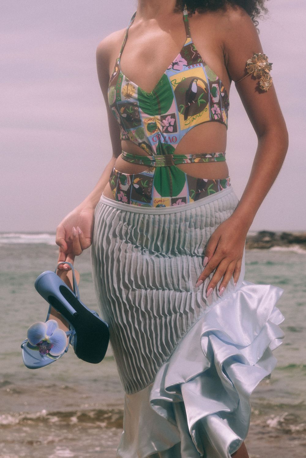 Close-up of striped skirt and tropical print top ensemble against coastal backdrop.