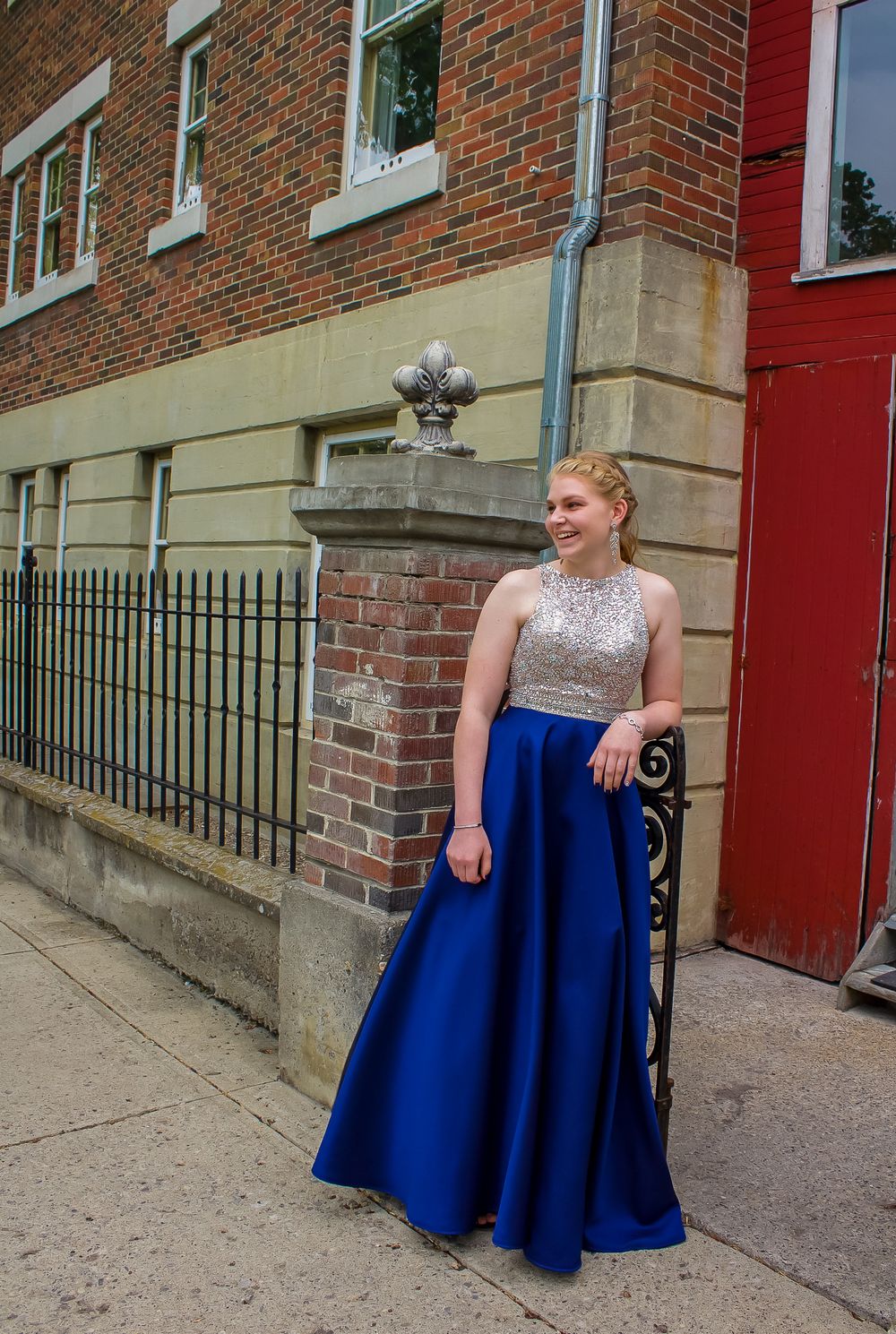 a grad in a deep blue & silver dress stands by a gate way.