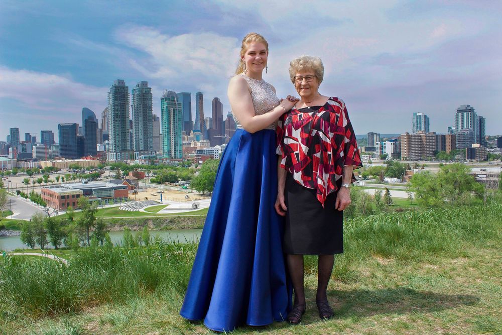 a grad stands with her grandmother, with a big city skyline behind them.