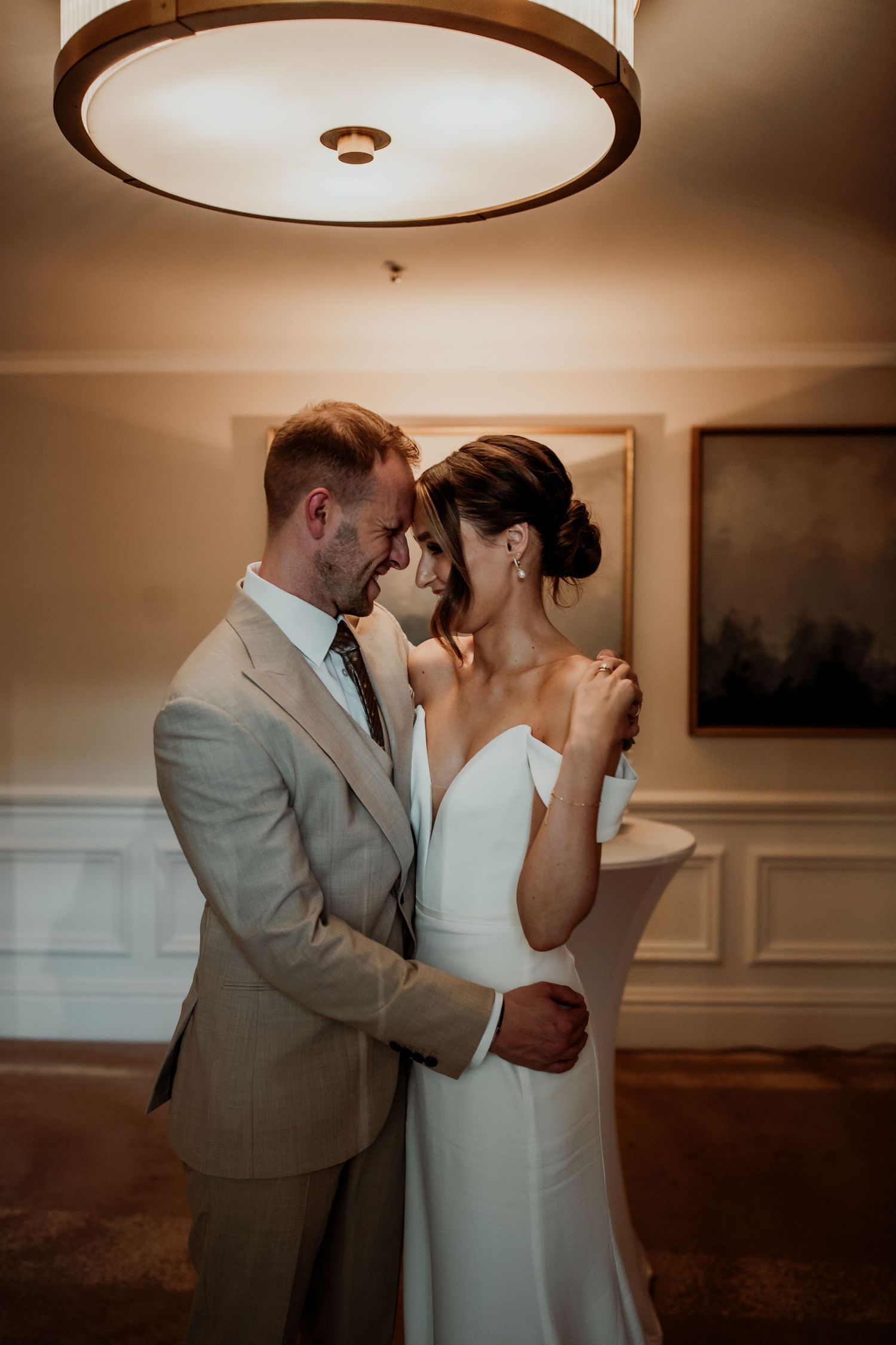 A romantic moment between newlyweds sharing an intimate embrace under warm lighting in an elegant indoor setting.