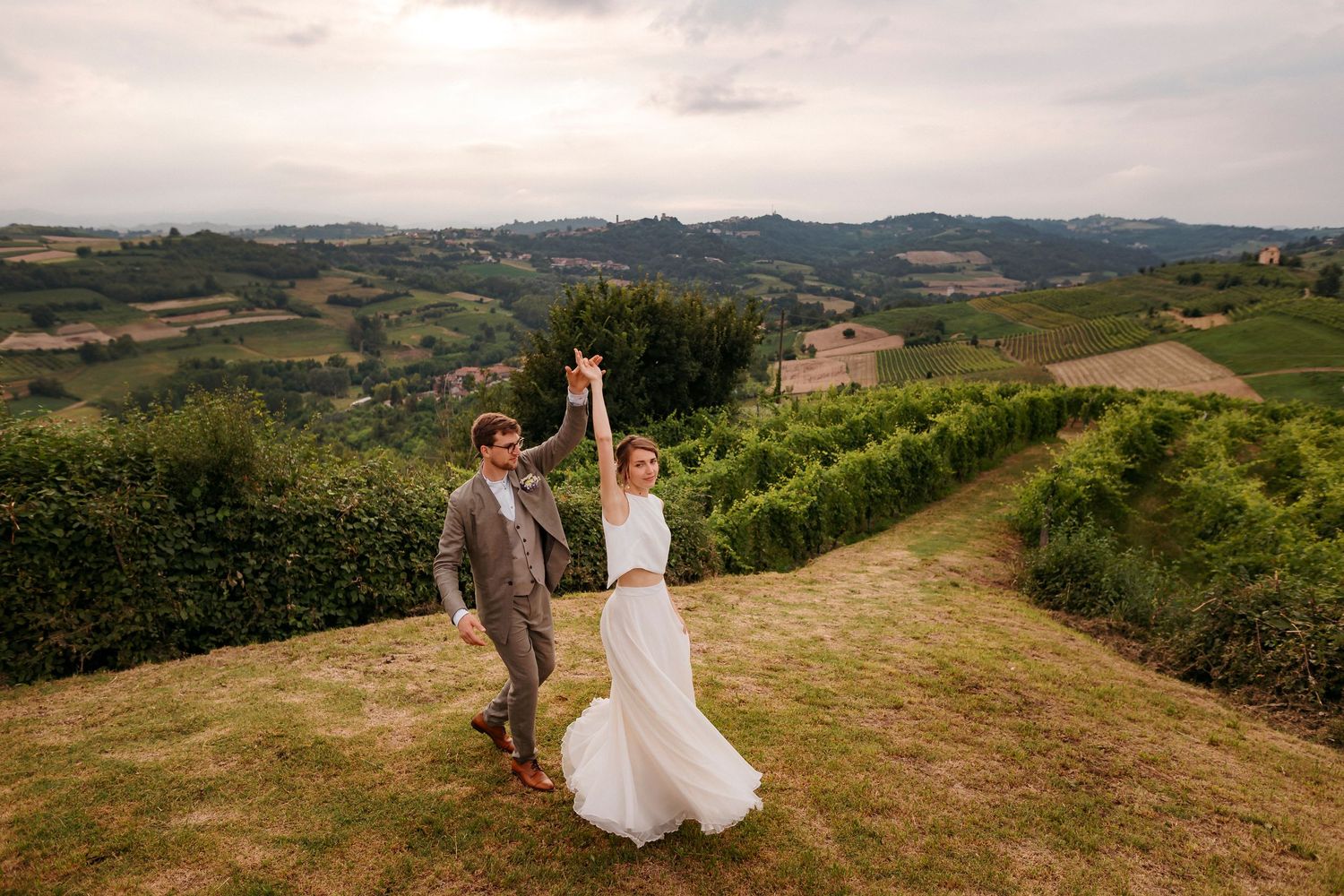 Newlyweds celebrate on a hilltop overlooking rolling countryside in Italy.