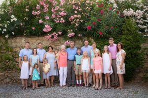A group in coordinated pastel outfits poses together in front of flowering bushes with pink blooms on a summer day.