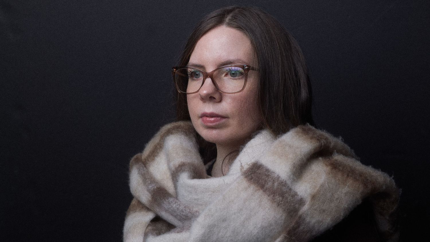 Portrait of person wrapped in cozy beige blanket against dark background.