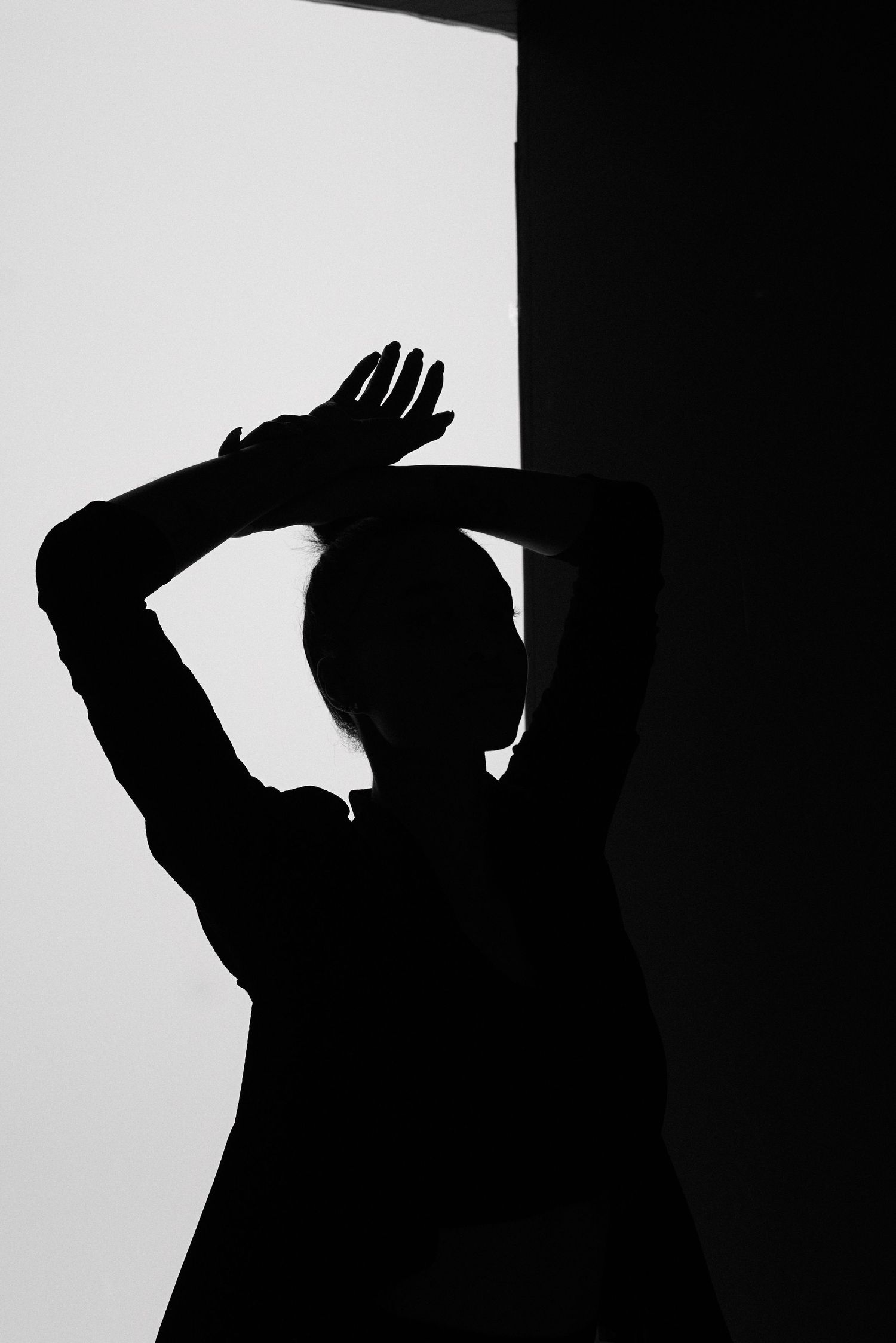 Dramatic silhouette of figure with raised arms against bright white background.