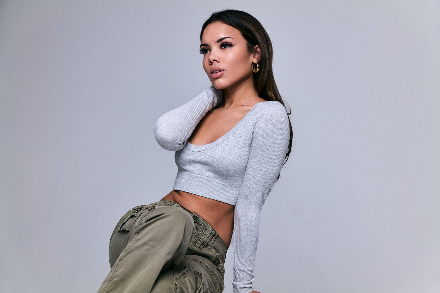 Fashion model in grey crop top and olive cargo pants poses against neutral background.