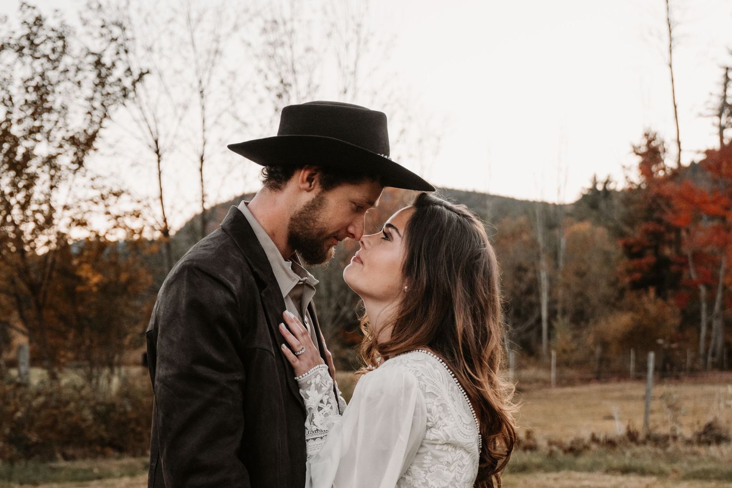 A romantic couple shares an intimate moment in a rustic autumn setting with fall foliage in the background.