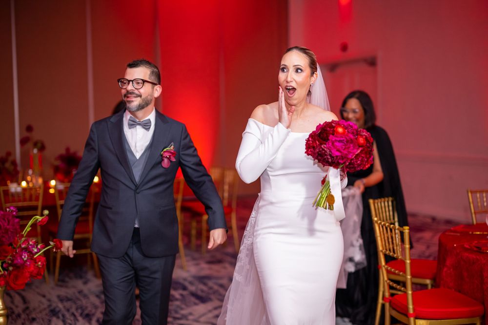 Wedding celebration in a red-lit reception room with formal attire and bright bouquet.