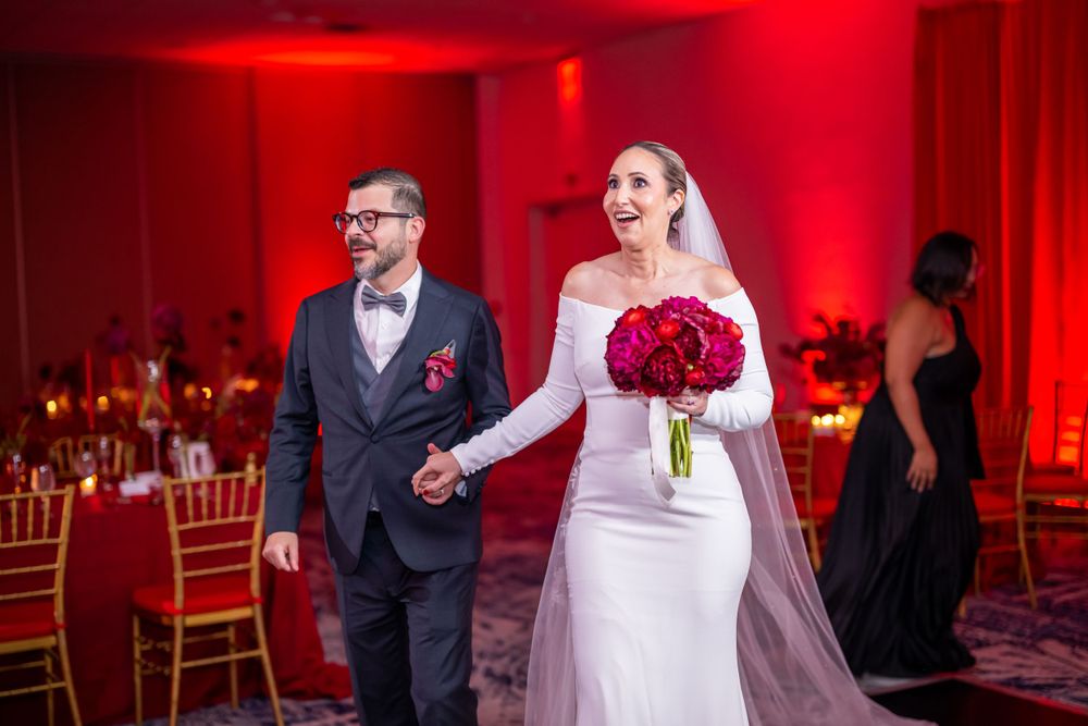 Couple entering their red-themed wedding reception with dramatic lighting.