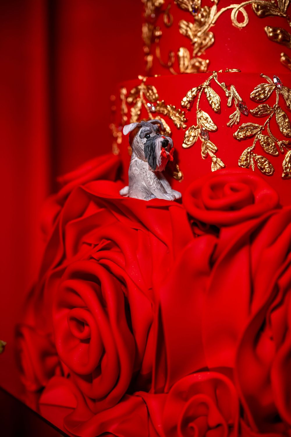 Close-up of wedding cake detail showing silver figurine against red roses and gold accents.