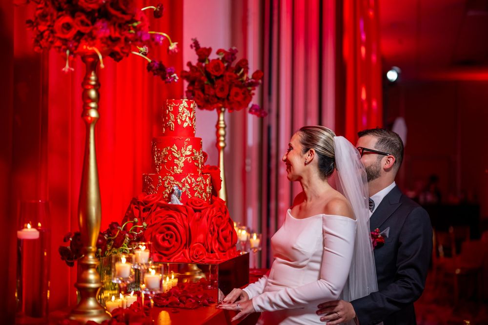 Wedding couple cutting their elegant red and gold tiered cake at their reception.