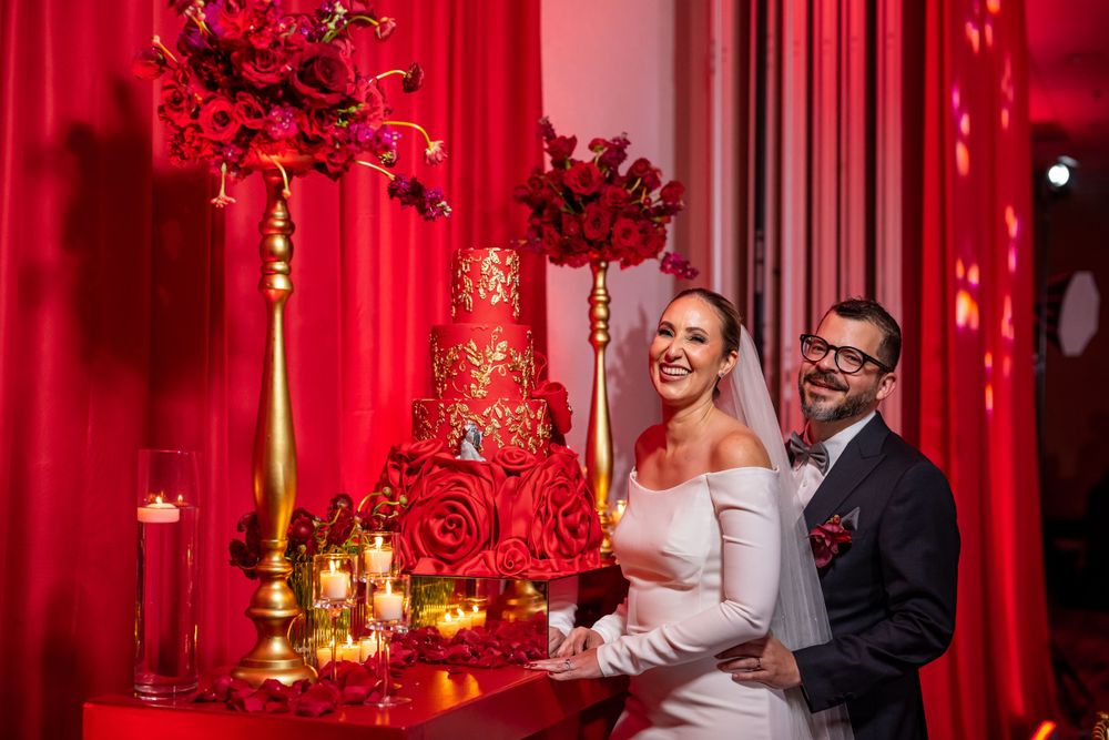 Elegant wedding reception decor features red drapery and floral centerpieces.