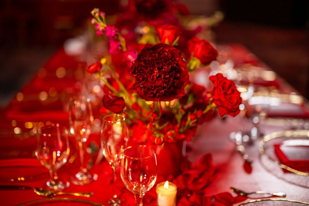 Elegant red wedding reception table with floral centerpieces and crystal glassware.