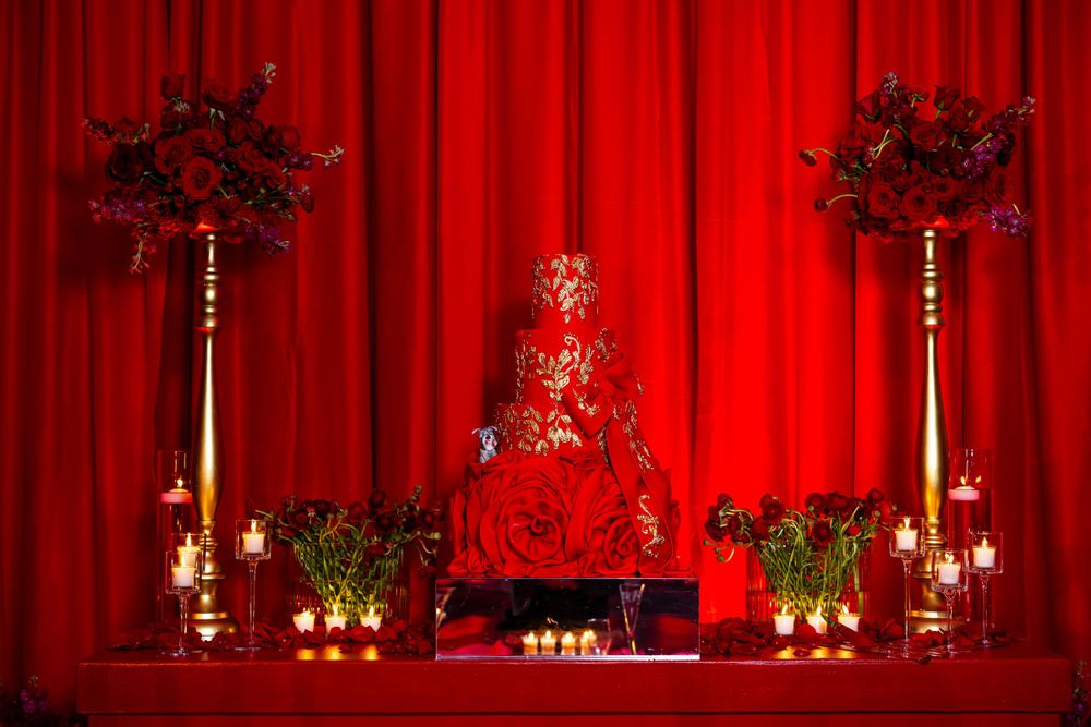 Dramatic red wedding cake display with floral arrangements and candlelight against red draping.