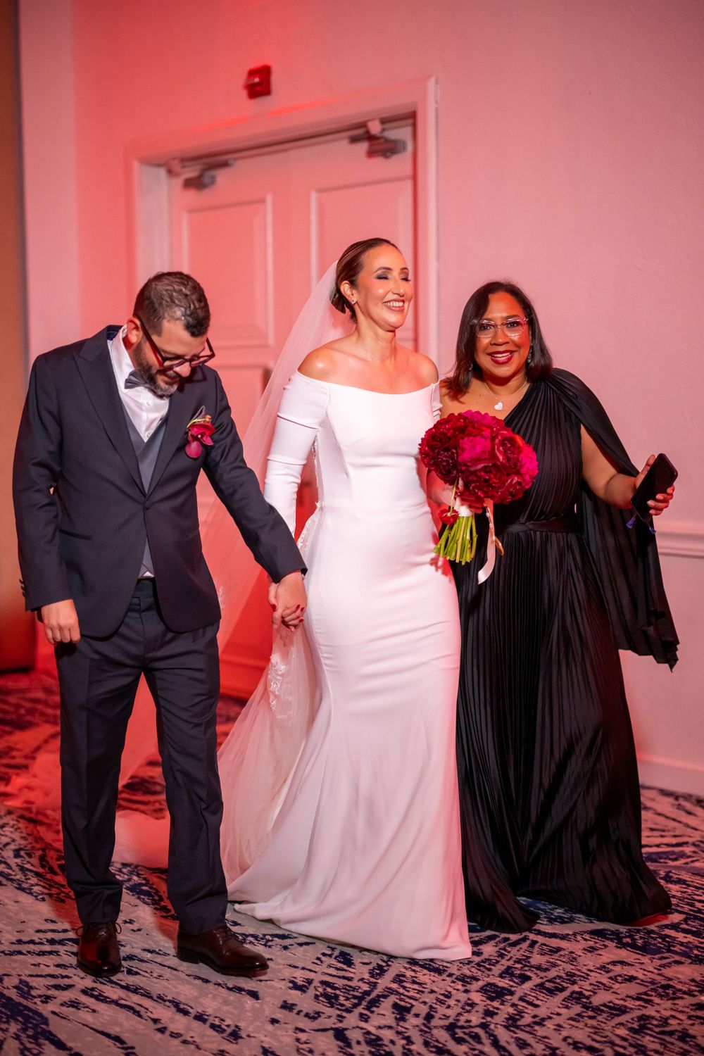 Wedding party members share a joyful moment in formal attire with red accents.