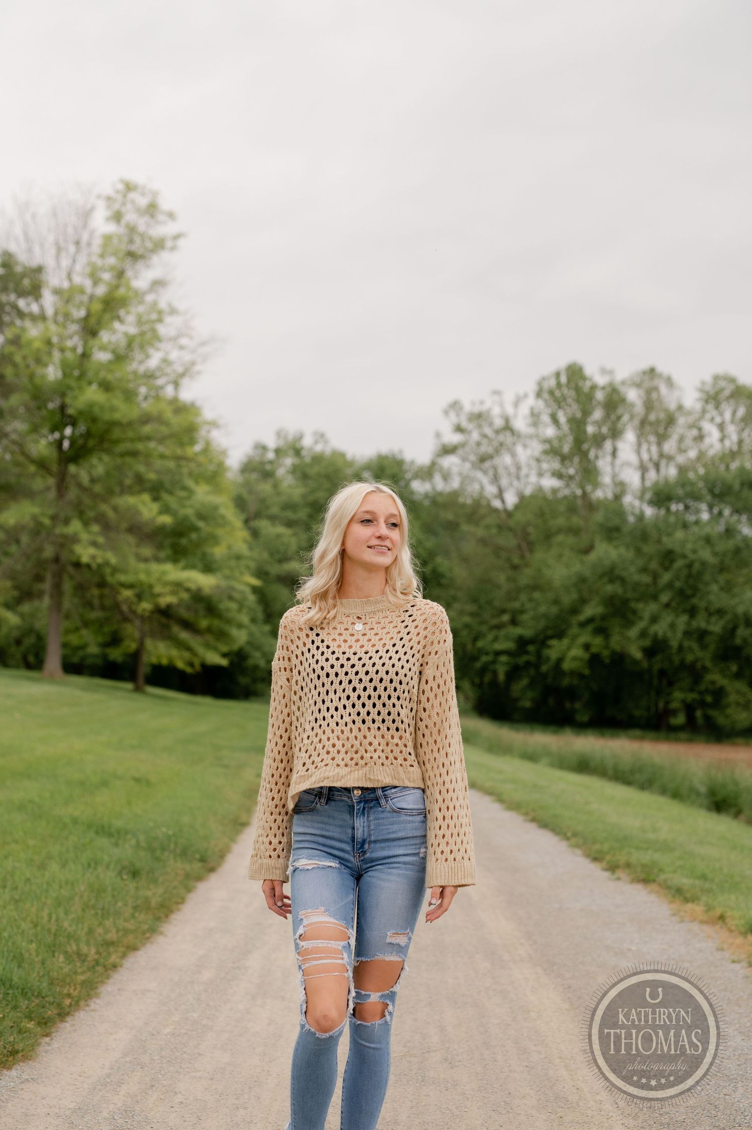 Stylish outdoor portrait on gravel path featuring beige crochet sweater and ripped jeans.