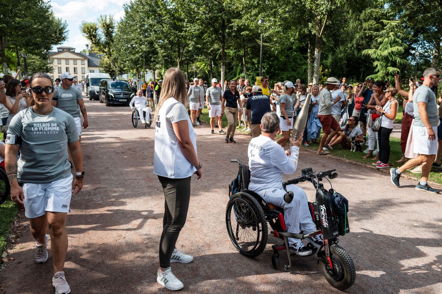 People enjoying a lively summer day on a tree-lined pedestrian walkway with a person in a wheelchair.