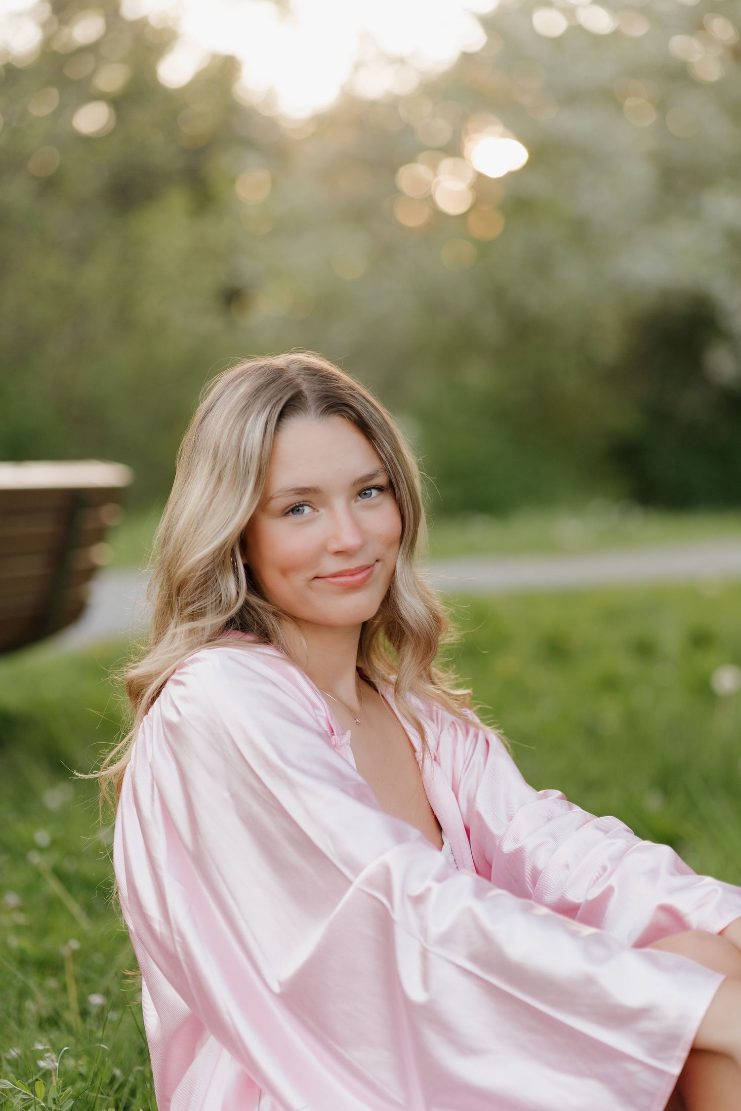 A woman in a pink satin blouse poses outdoors in a series of natural portraits at sunset.