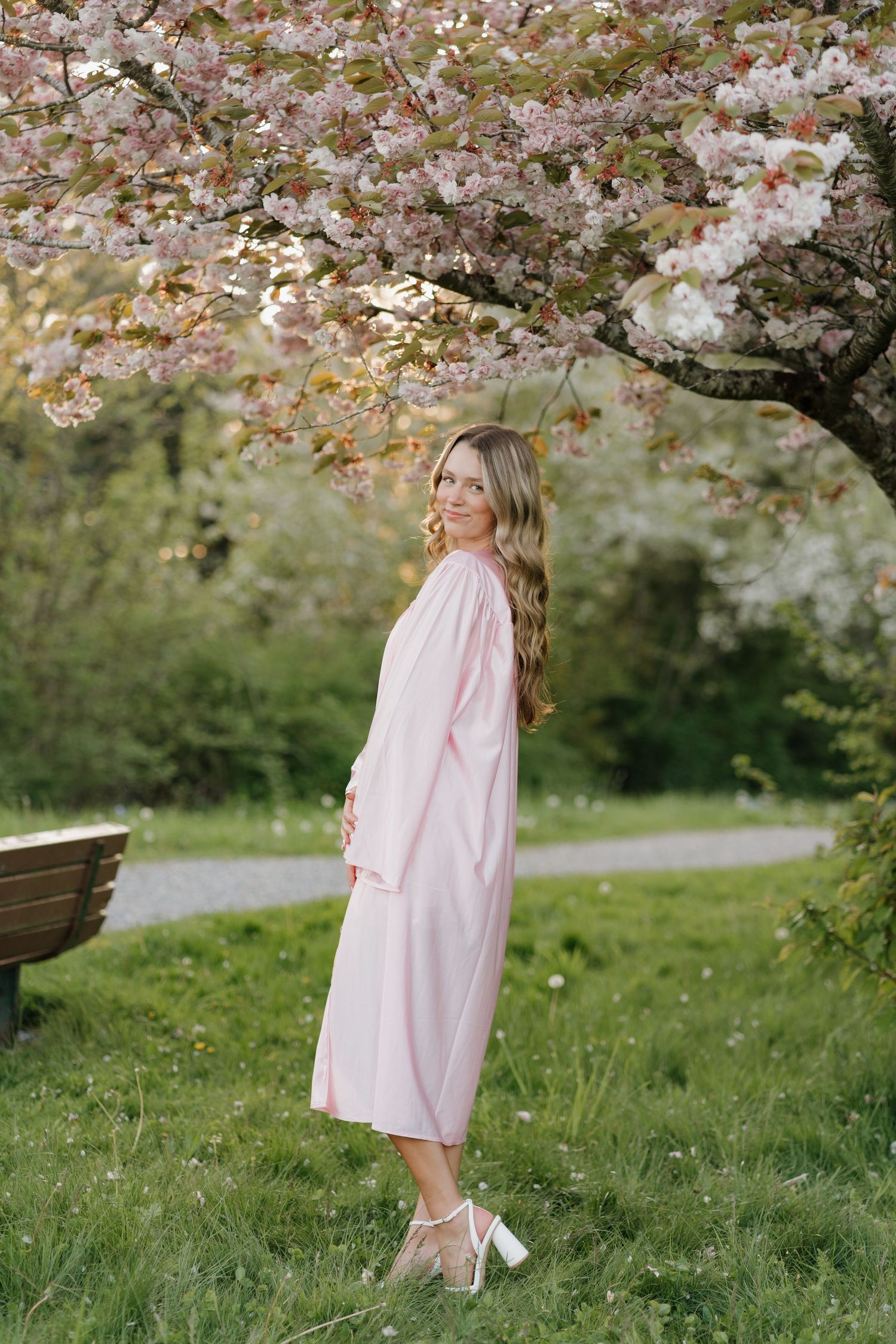 Figure in flowing pink dress twirls under cherry blossom trees in a serene garden setting.