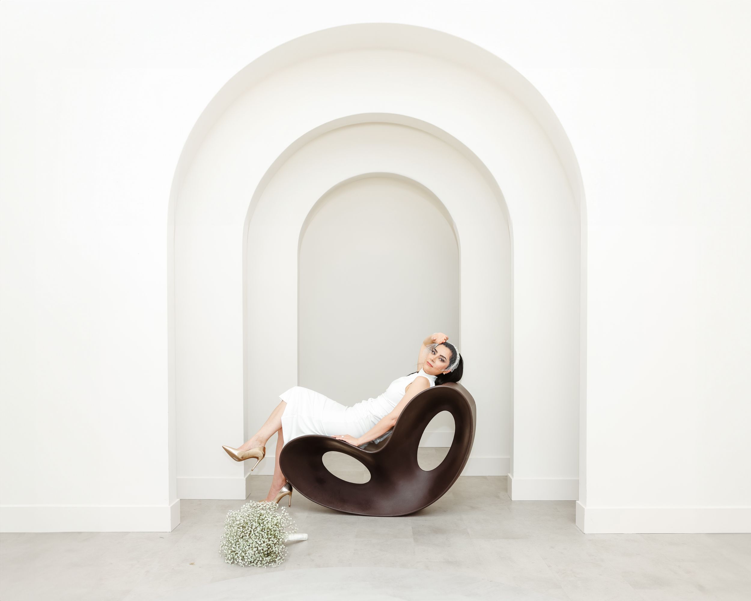 Artistic bridal portrait in curved white archway with modern sculptural seat.