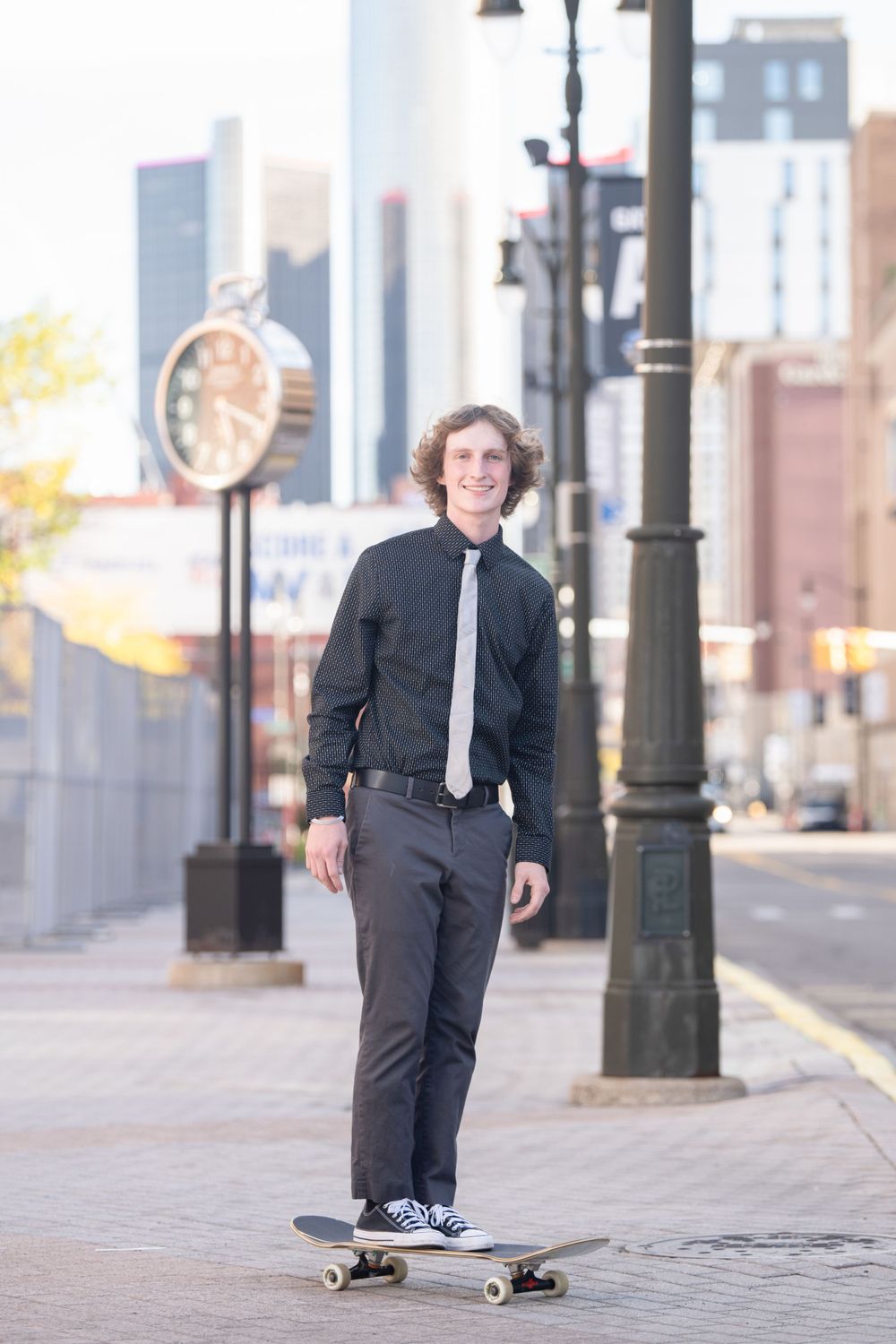 Person in dark formal attire skateboarding on city sidewalk.