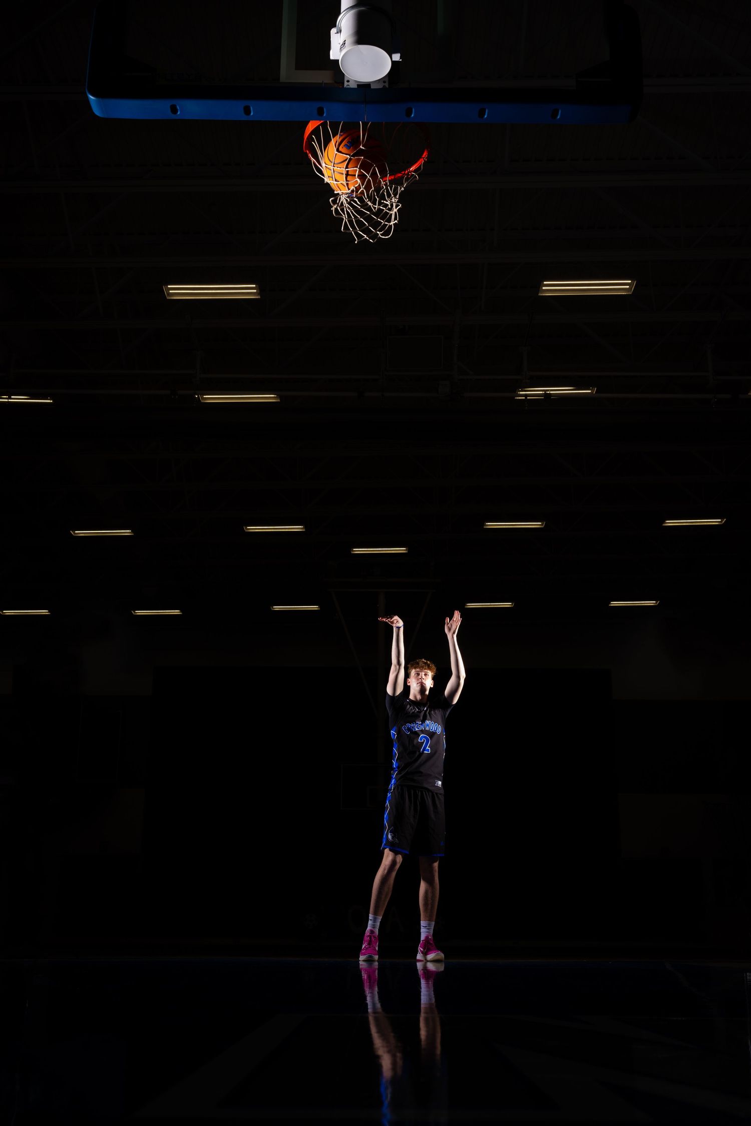 Silhouetted basketball player jumping in dark gym with illuminated hoop above.