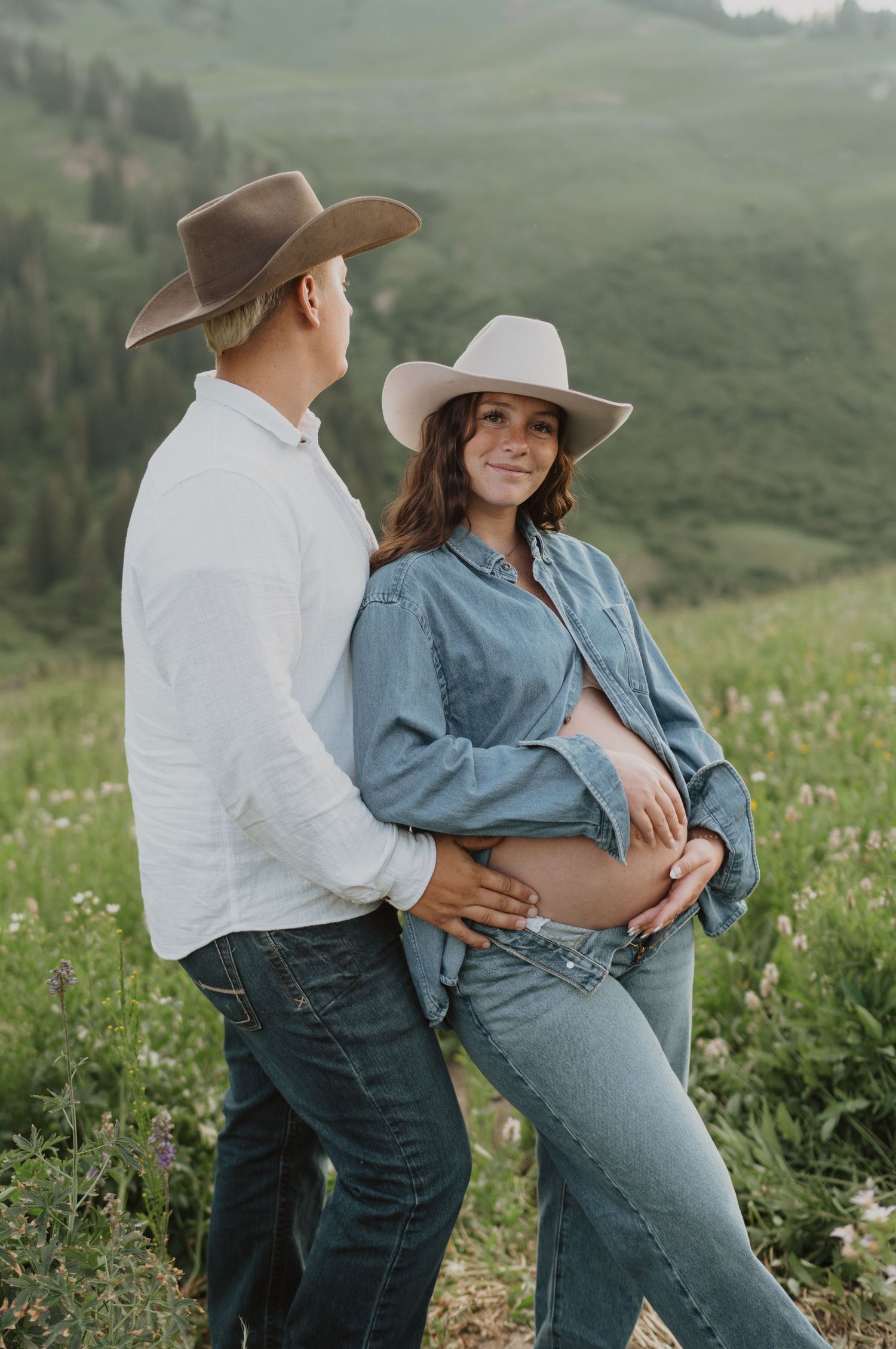 Maternity photos of couple in western wear posing in mountain wildflower field.
