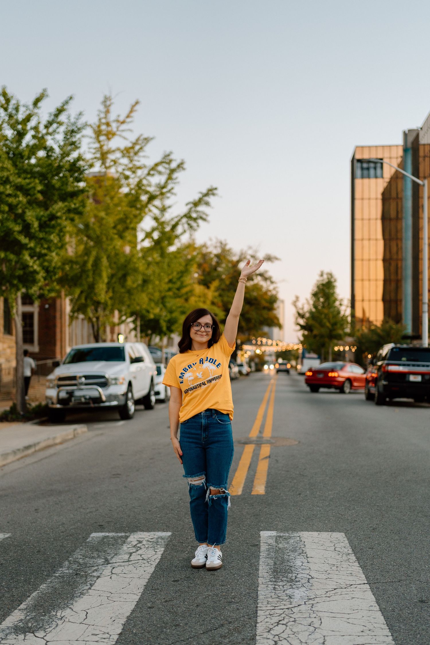 Person in yellow shirt and jeans posing playfully on a crosswalk with buildings in background. Chattanooga Senior Photographer