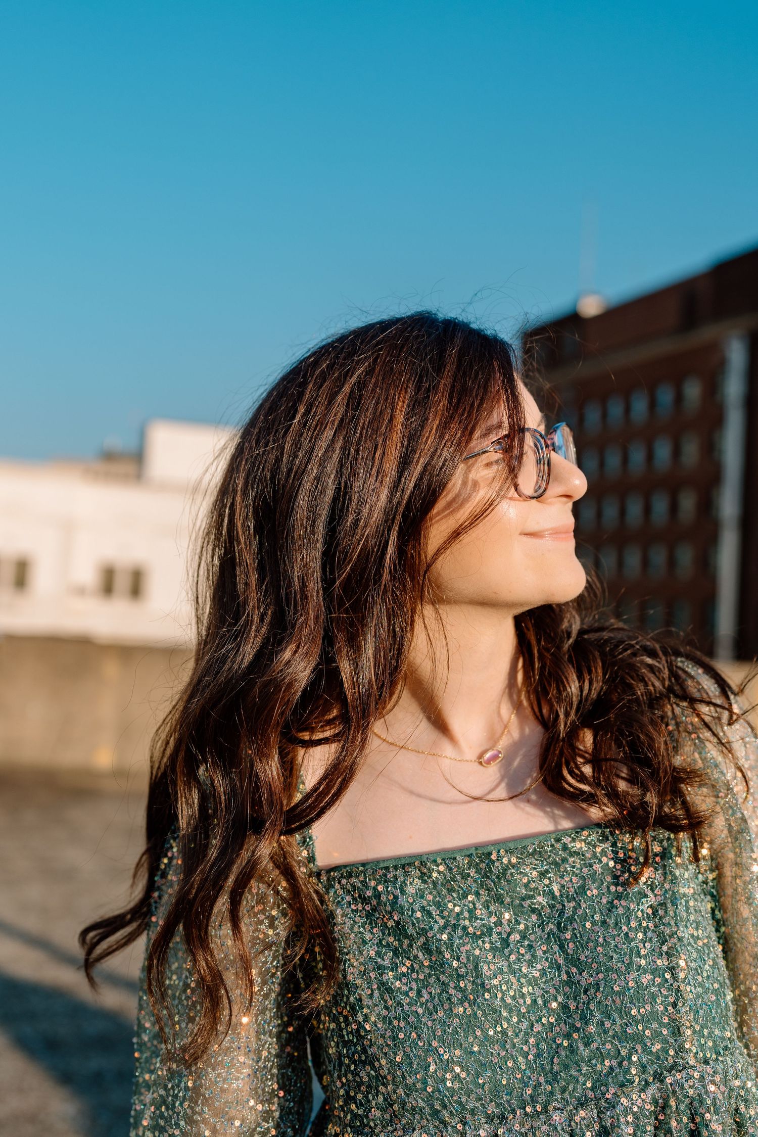 Person with flowing hair in sparkly dress poses against bright blue sky on rooftop. Chattanooga Senior Photographer