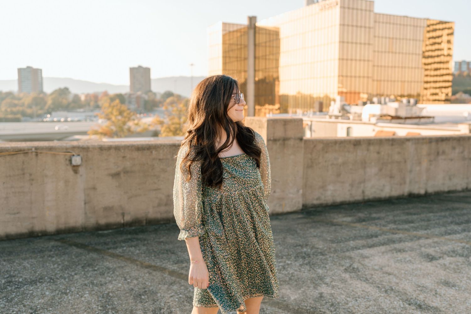 A woman in a green dress twirls on a rooftop with city buildings in the background. Chattanooga Senior Photographer