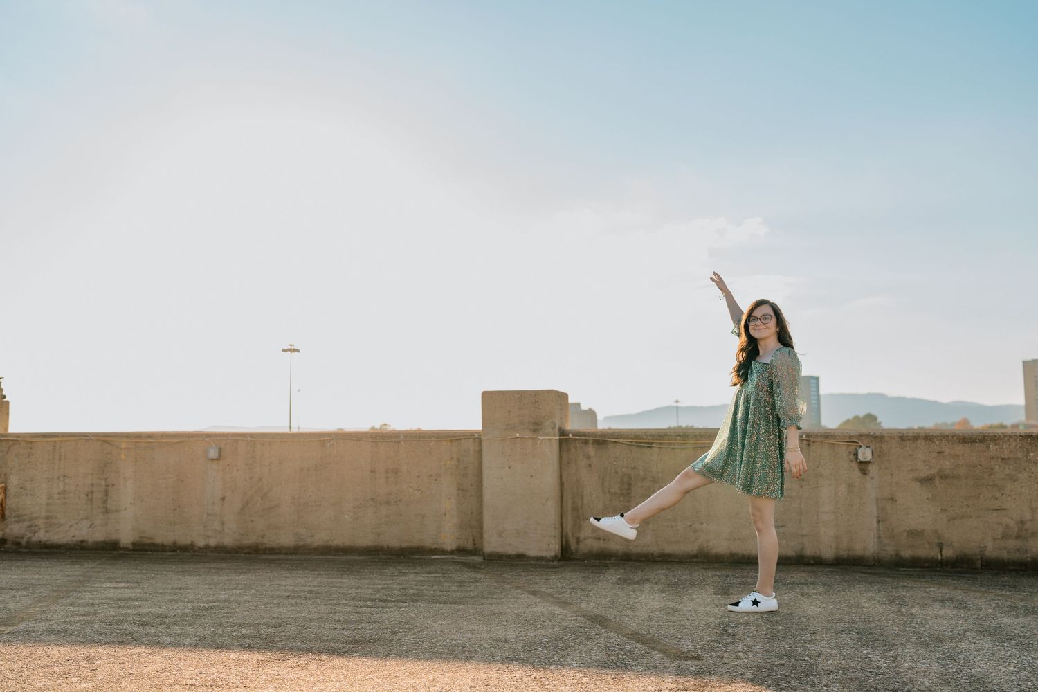 Person in casual outfit poses joyfully against bright sky on urban rooftop. Chattanooga Senior Photographer
