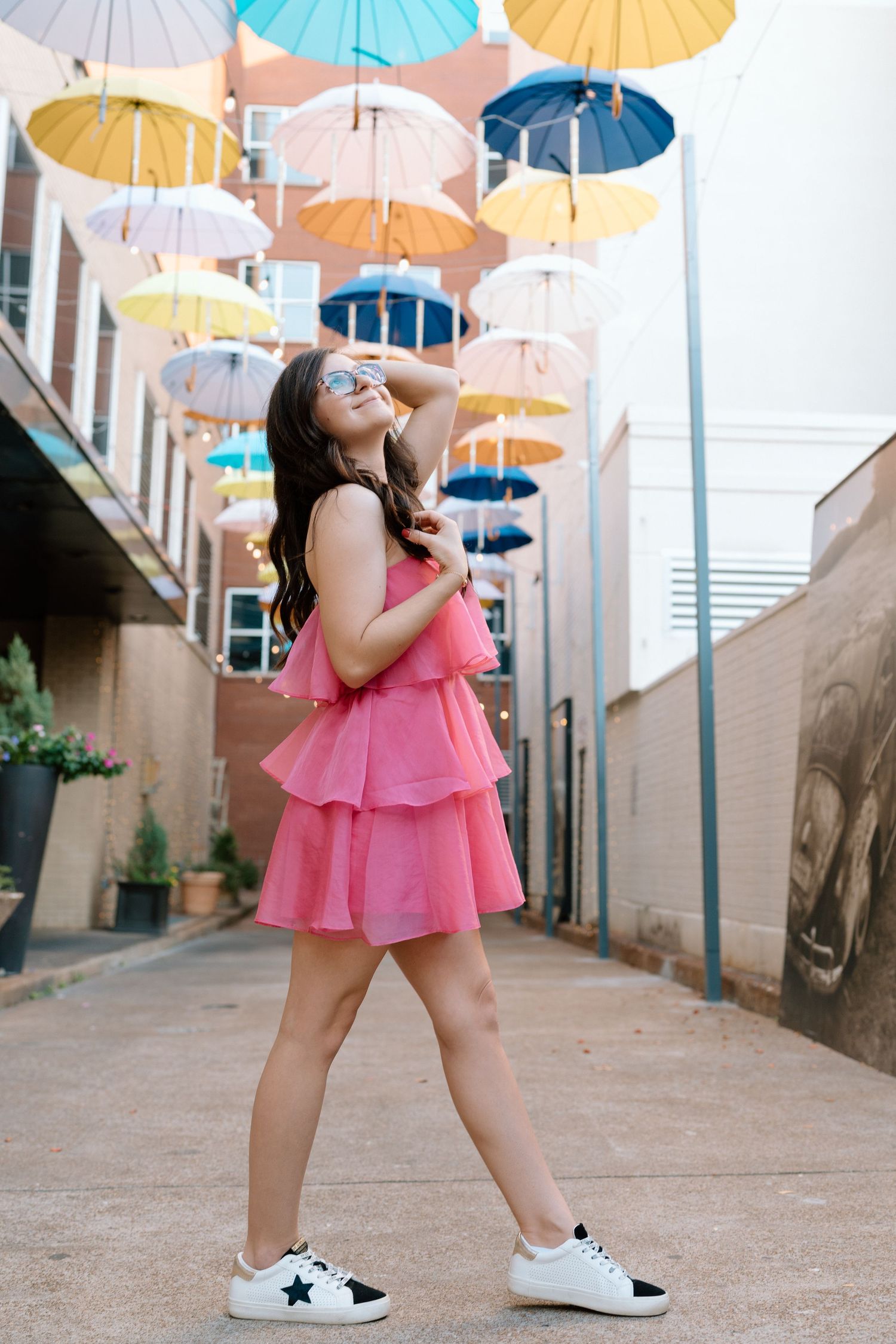 Person in pink dress dances under colorful hanging umbrellas in urban alleyway. Chattanooga Senior Photographer