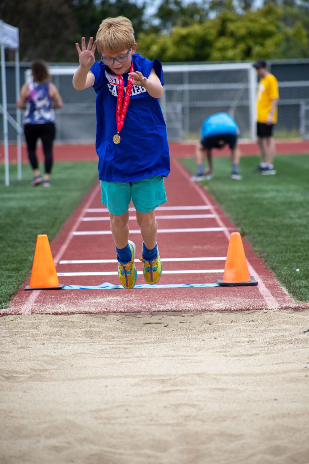 Young athlete in blue shirt and teal shorts practices long jump technique between orange cones on track.