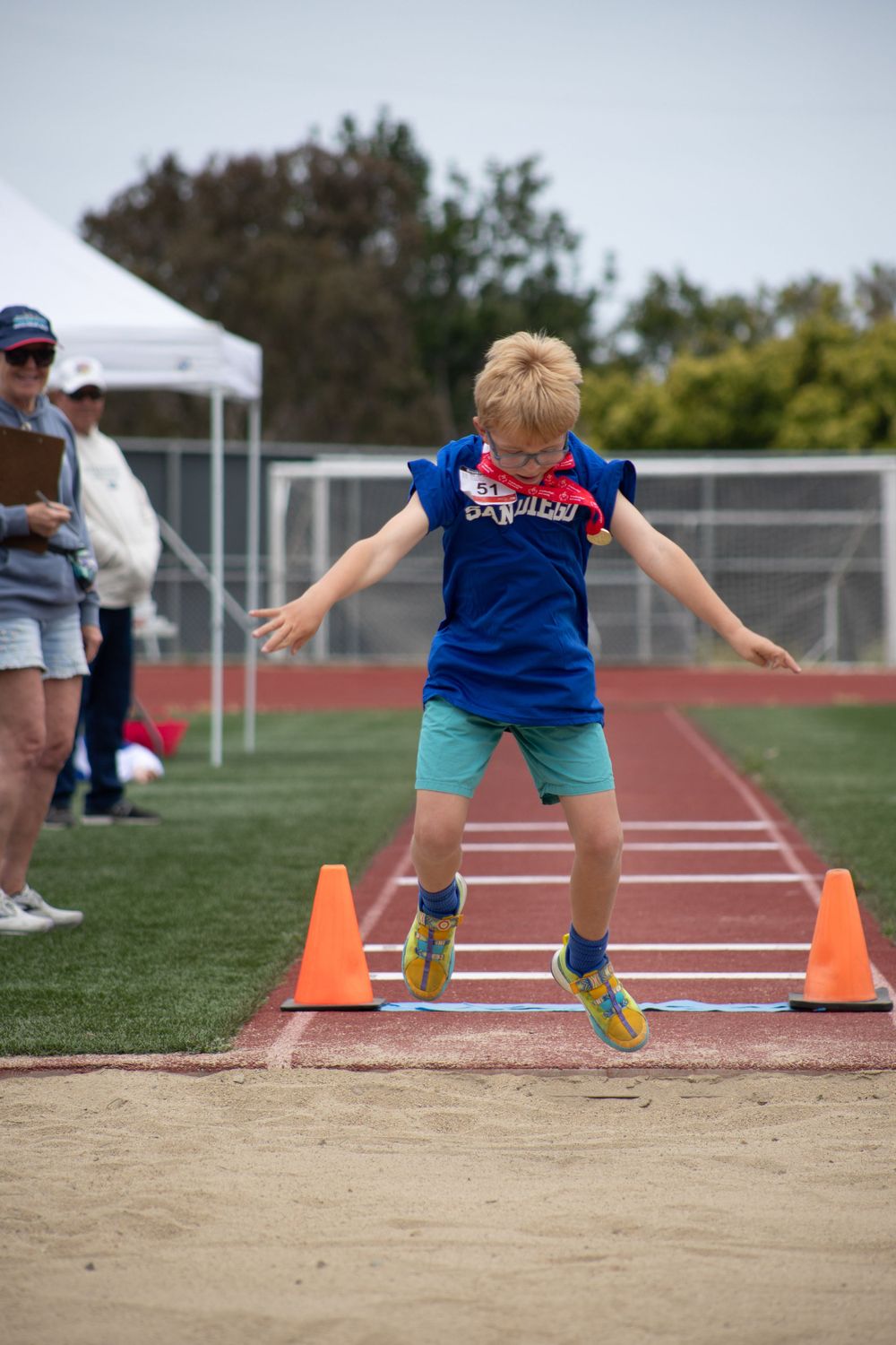 Athlete in blue shirt and shorts practices jumping form at an outdoor track field.