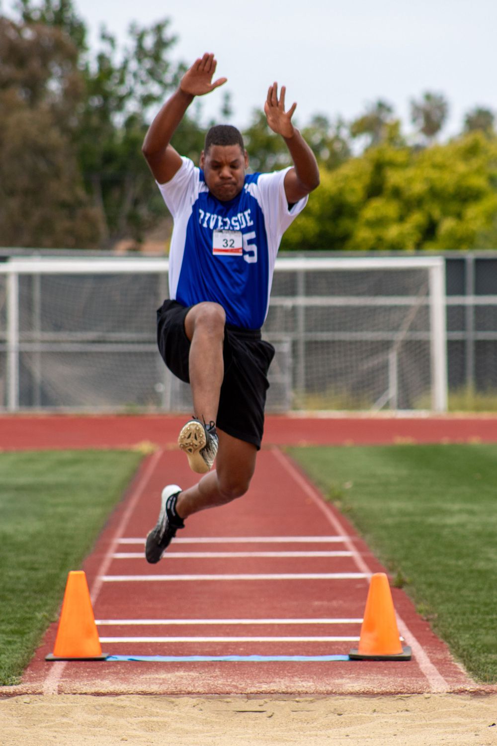 Track athlete in blue jersey executes powerful long jump motion during competition.